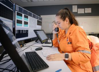 Two production engineers, wearing high visibility workwear, sitting at their workspaces and reviewing data. 