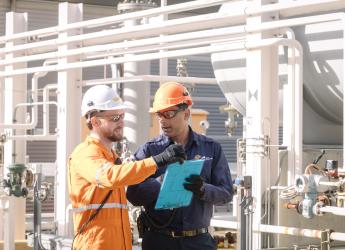 Two engineers at a plant facility, reviewing documents on a clipboard. 