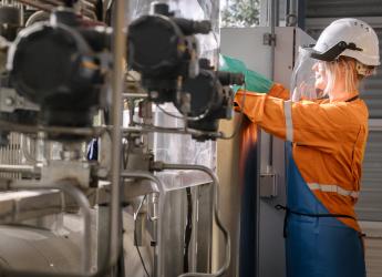 A female engineering production worker, wearing protective workwear and treating chemicals.