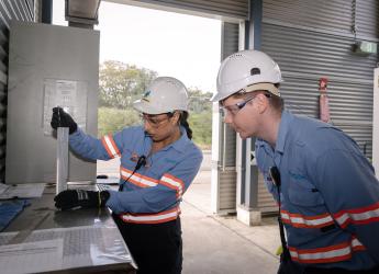 Two chemistry technicians, wearing high visibility workwear, observing samples. 
