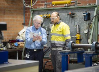 Two metal fitters reviewing documents in a workshop. 