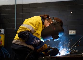 A female welder, wears a welding mask while she welds steel beams in a workshop. 