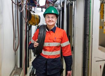 A technical cable jointer, wearing high visibility workwear and holding a roll of cable. 